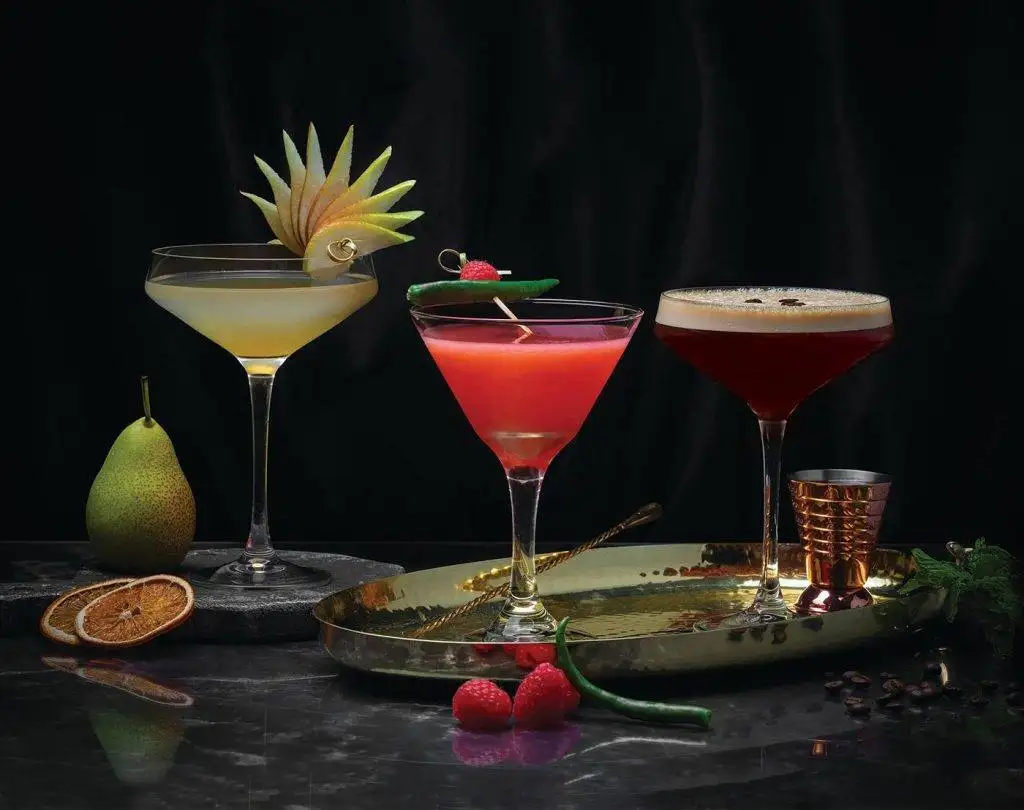 Elegant trio of infused martinis at Asha's Restaurant featuring pear, raspberry, and espresso variations with fresh fruit garnishes on dark marble