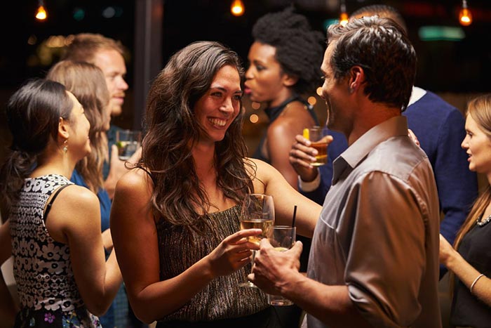Group of elegantly dressed people enjoying drinks and conversation at an intimate private party, with ambient lighting creating a sophisticated atmosphere